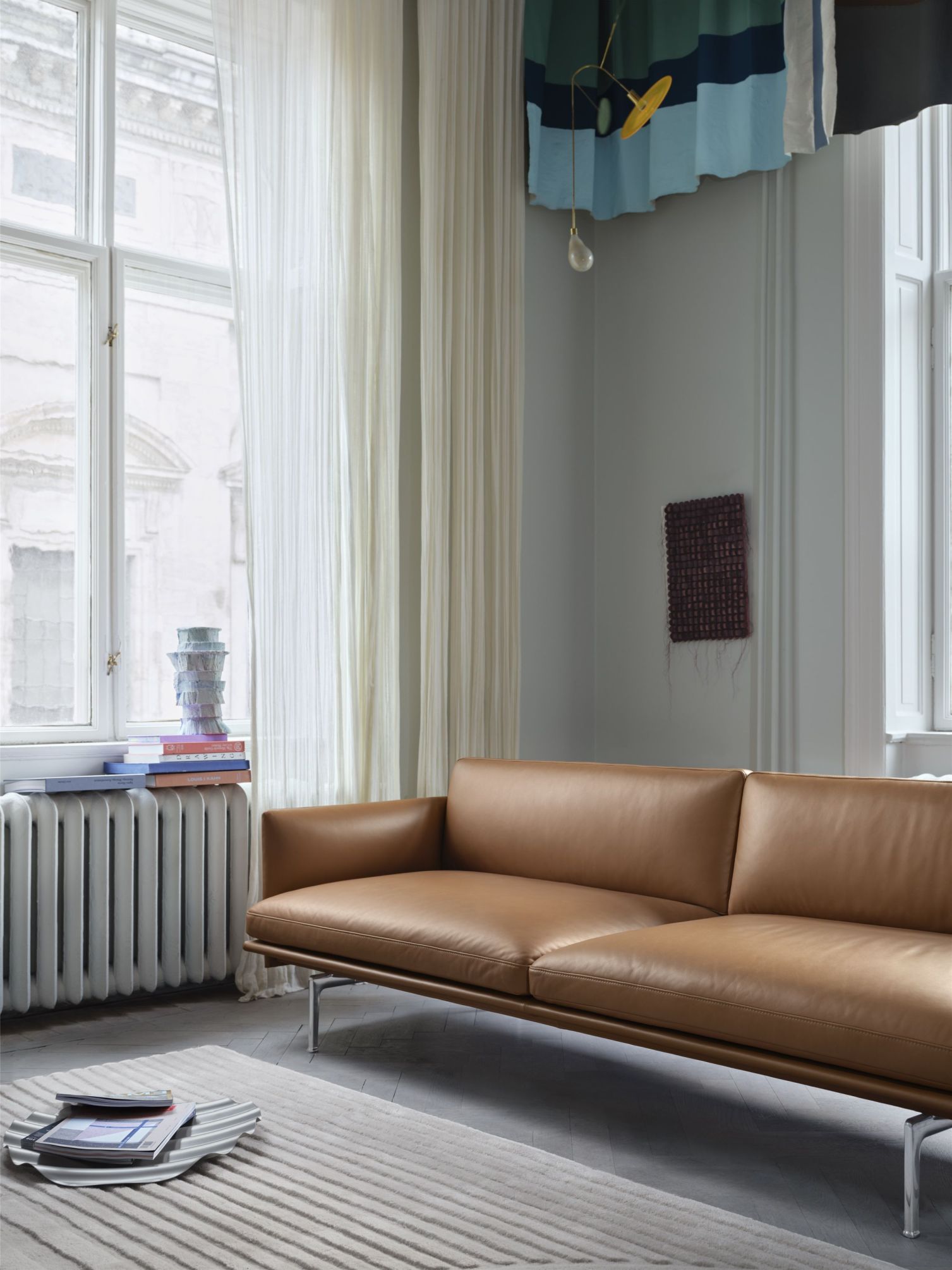 Helles Wohnzimmer mit modernem, braunen Ledersofa auf einem gestreiften Teppich vor einem Fenster.