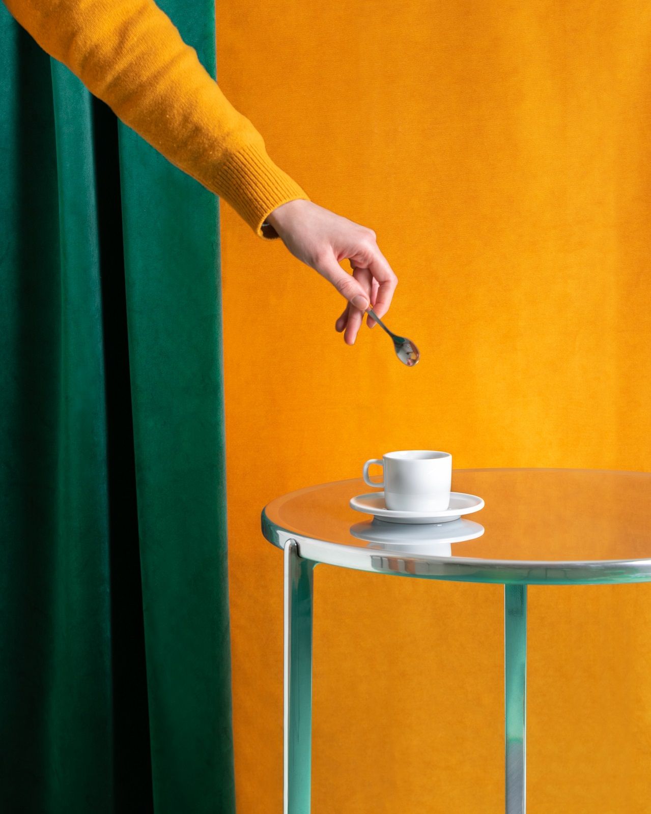 Tambour Beistelltisch von Magis mit Kaffeetasse und Hand mit Löffel vor farbigem Hintergrund.