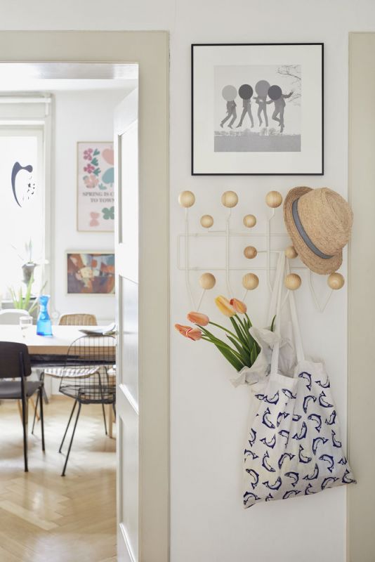 Weiße Garderobe mit Holzkugeln, Hut, Tulpen in Stofftasche mit Delfinmuster an einer weißen Wand.