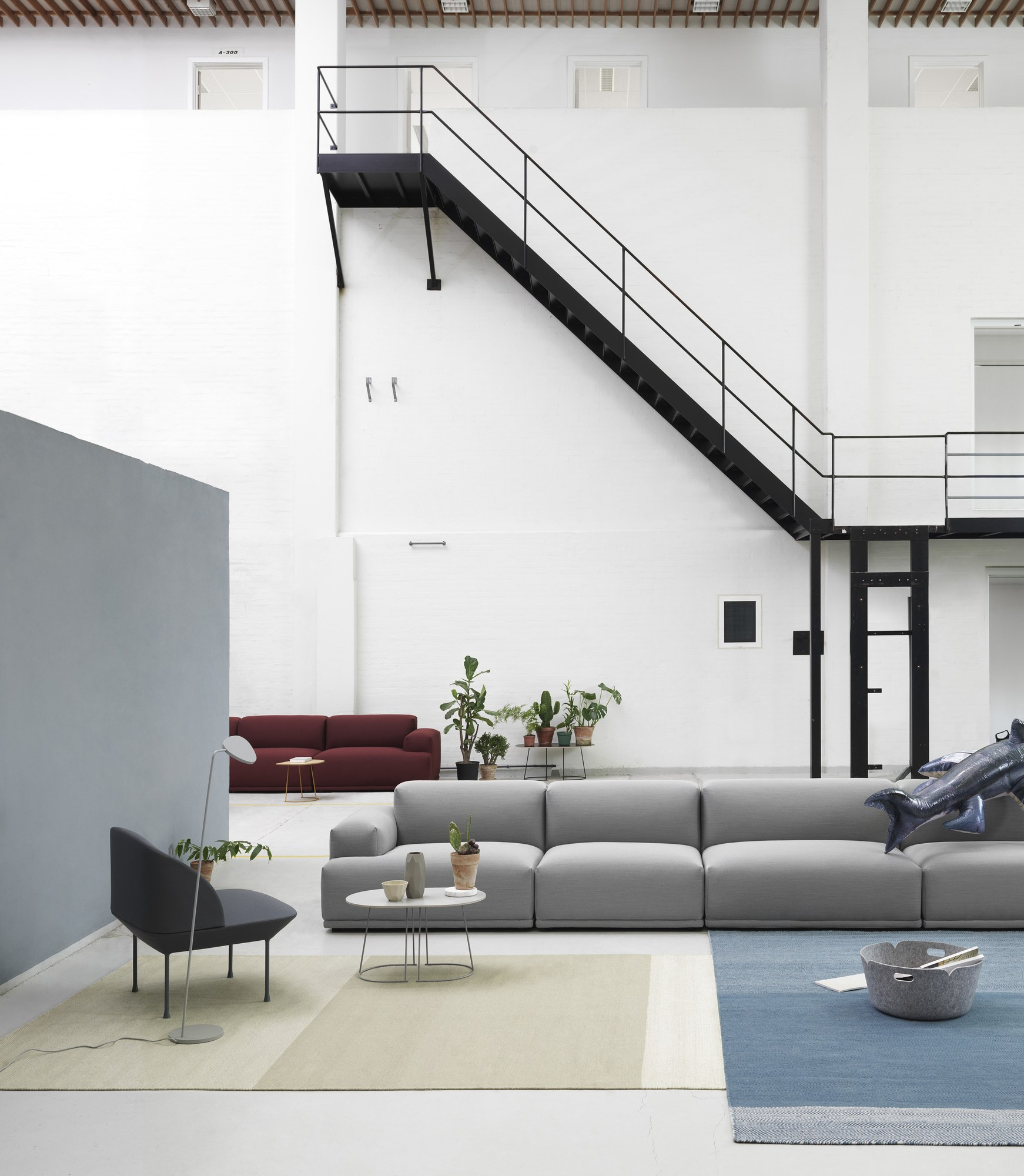 Heller Raum mit Muuto Varjo Teppich in Beige und Blau, grauer Couch und Treppe.