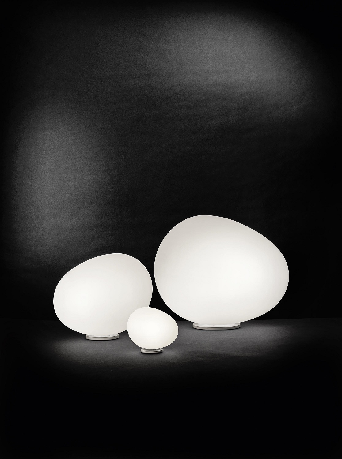 Drei weiße Gregg Tischleuchten von Foscarini in verschiedenen Größen vor schwarzem Hintergrund.