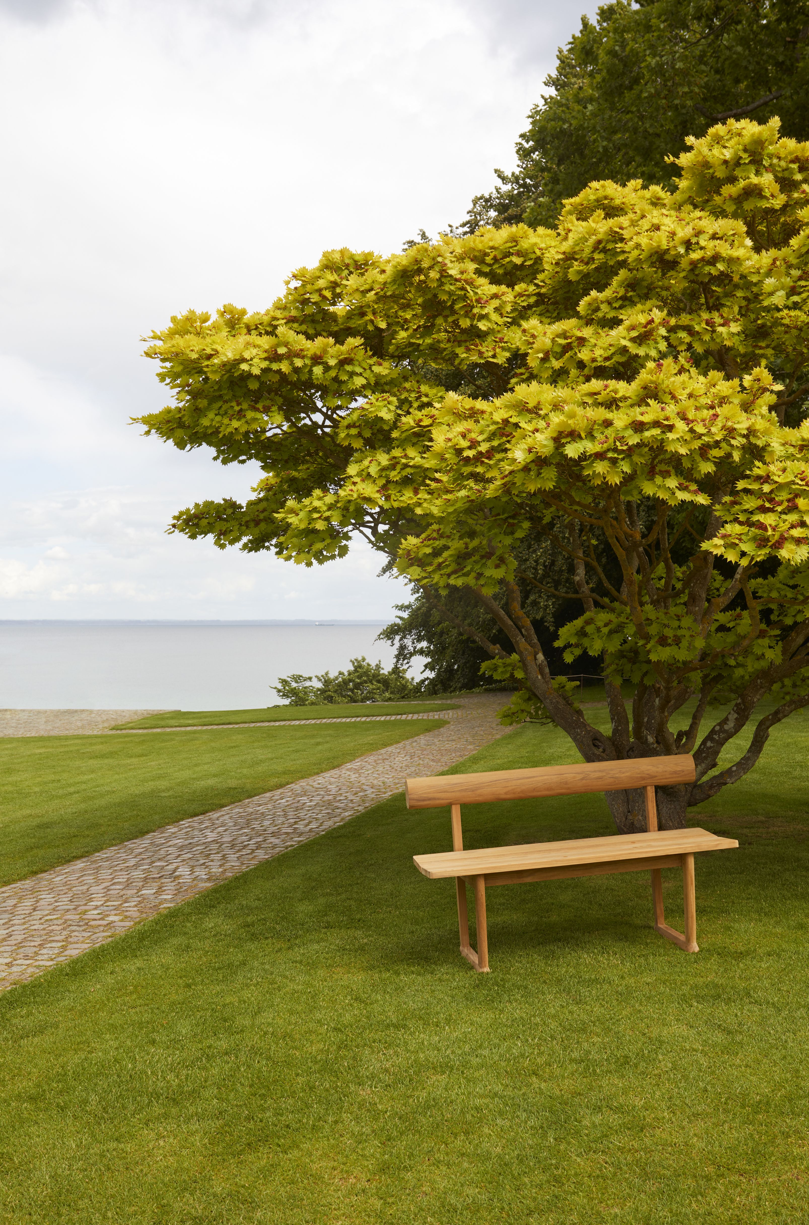 Banco Bank aus Teakholz von Skagerak by Fritz Hansen im Garten mit Meerblick.