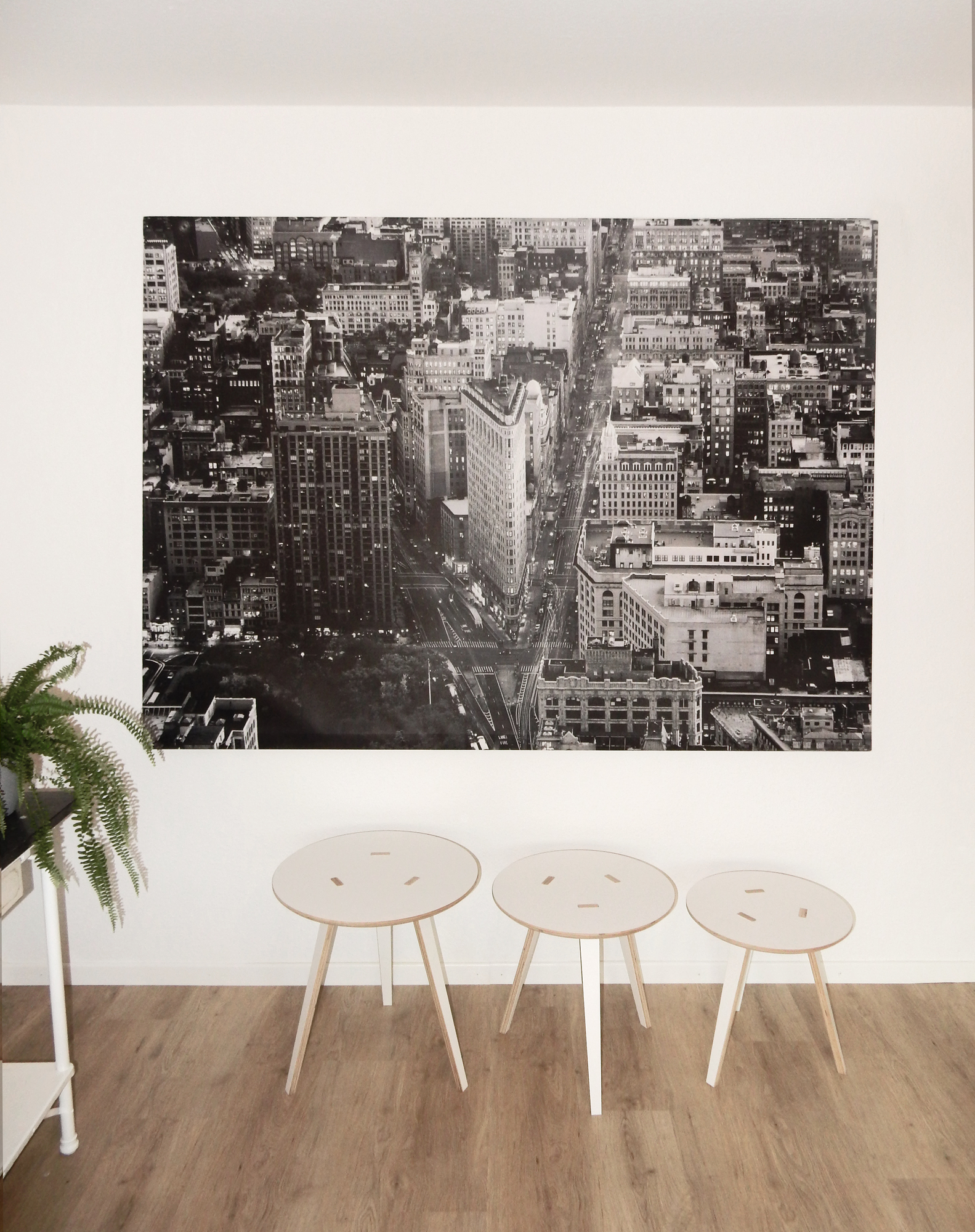 Drei Tojo Rund Tische 500 aus Holz vor einer Wand mit New York Bild.