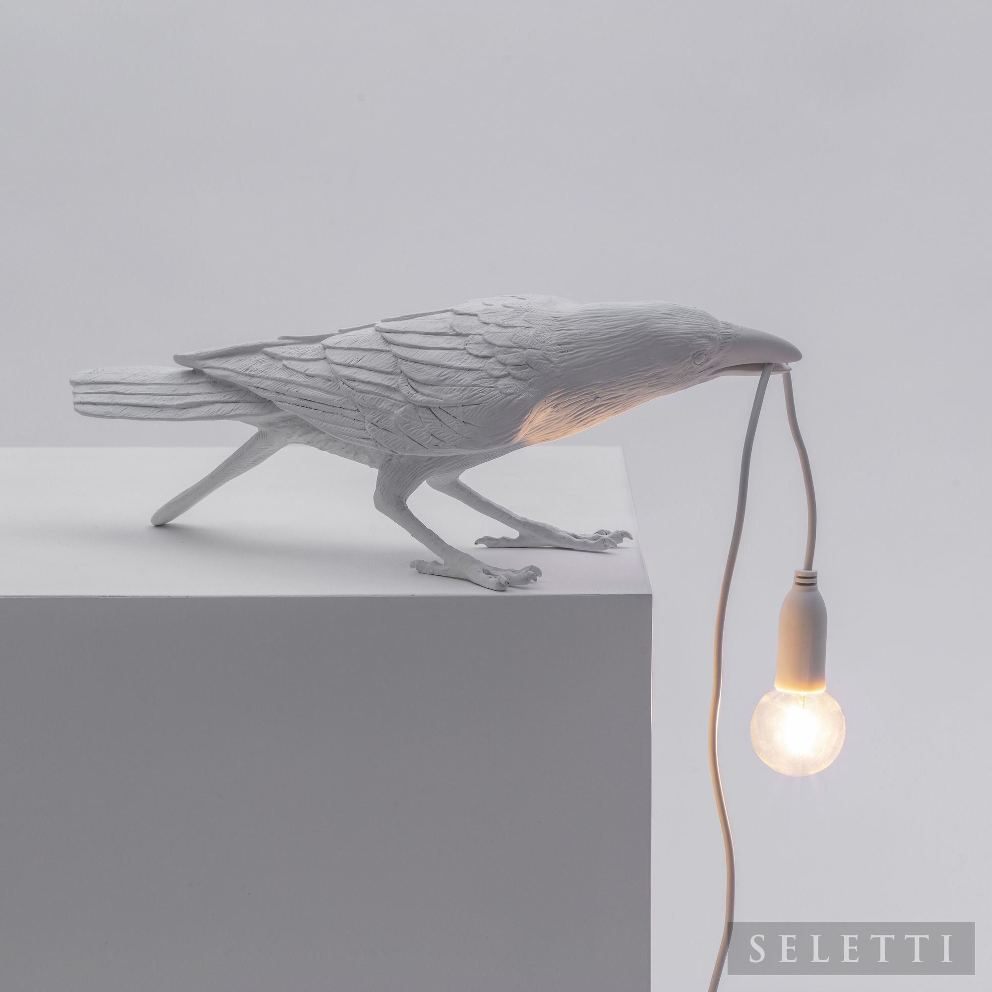 Weiße Bird Lamp Playing Leuchte von Seletti: Detailaufnahme einer Krähen-Tischleuchte, die ein Leuchtmittel im Schnabel hält.