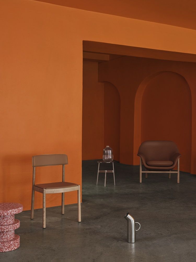Innenaufnahme mit einem braunen Normann Copenhagen Lounge Sessel und weiteren Möbeln vor orangefarbenen Wänden.