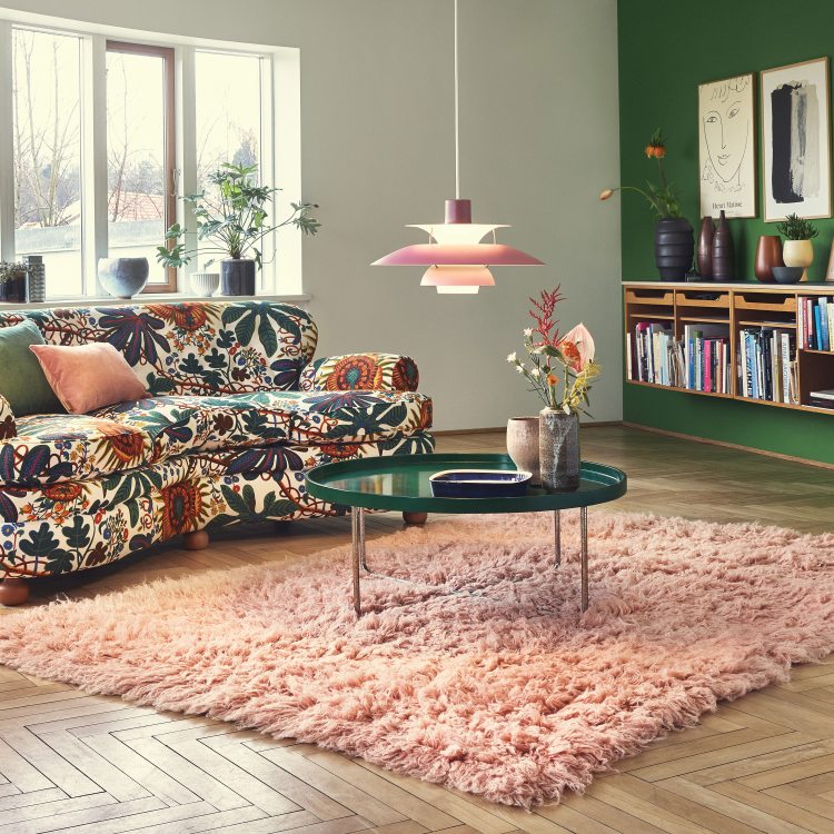 Rosa PH 5 Pendelleuchte von Louis Poulsen über einem Wohnzimmer mit Teppich und Sofa.