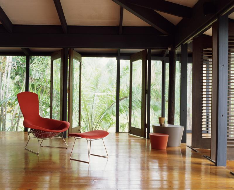 Roter Bertoia Hochlehner Sessel mit Fußhocker von Knoll International vor Fensterfront mit Grünblick.