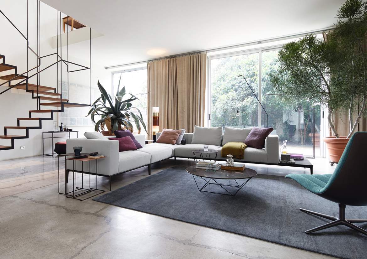 Helles Wohnzimmer mit modernem Ecksofa, grauem Teppich, Designertisch und Treppe. Hochwertige Möbel für stilvolles Wohnen.