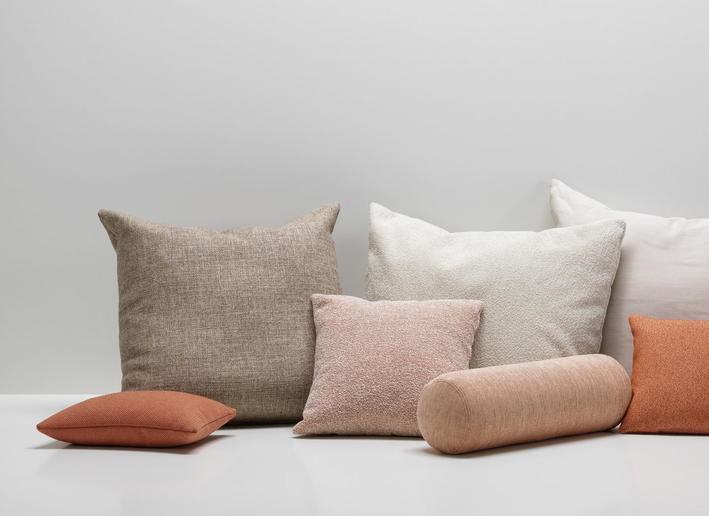 Vitra Cushions: Gruppe von verschiedenen Zierkissen und Sofakissen in Beige-, Weiß- und Rosatönen auf weißem Untergrund.