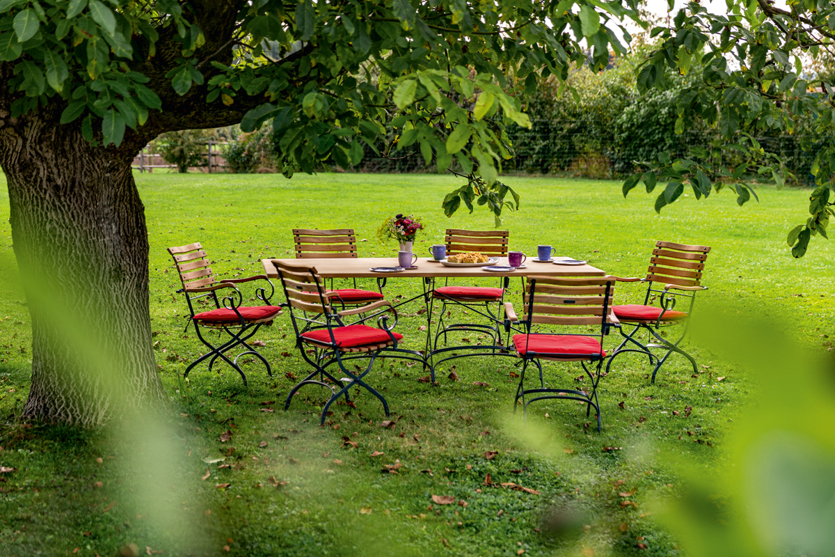 Weishäupl Classic Armchair Sessel, graphitgrau, klappbar, mit Armlehnen und roten Sitzkissen im Garten.