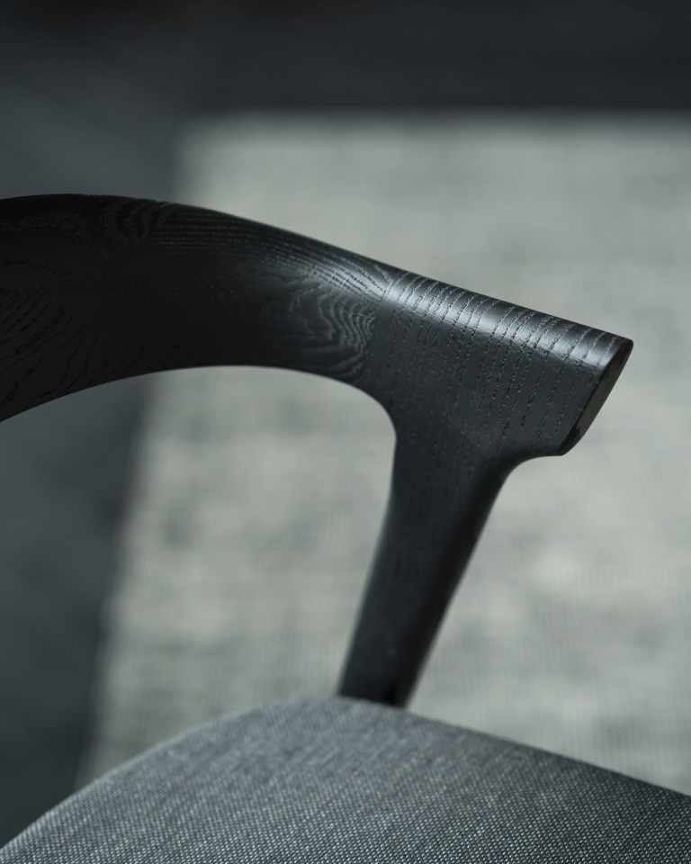 Detailaufnahme des Bok Stuhls von Ethnicraft: Schwarze Eichenholz-Armlehne und grauer Stoffbezug.
