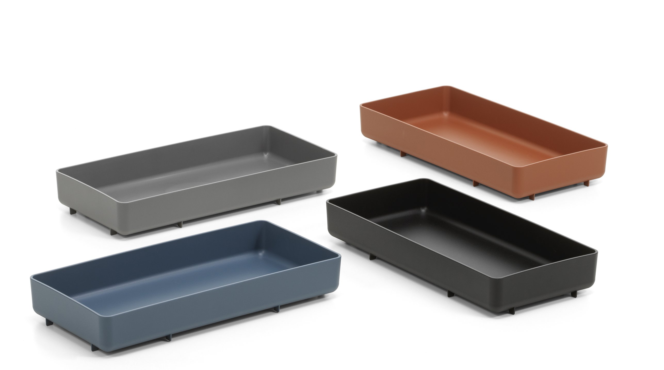 Vier Chap Tray Tabletts von Vitra in Dunkelgrau, Schwarz, Blau und Braun auf weißem Hintergrund.