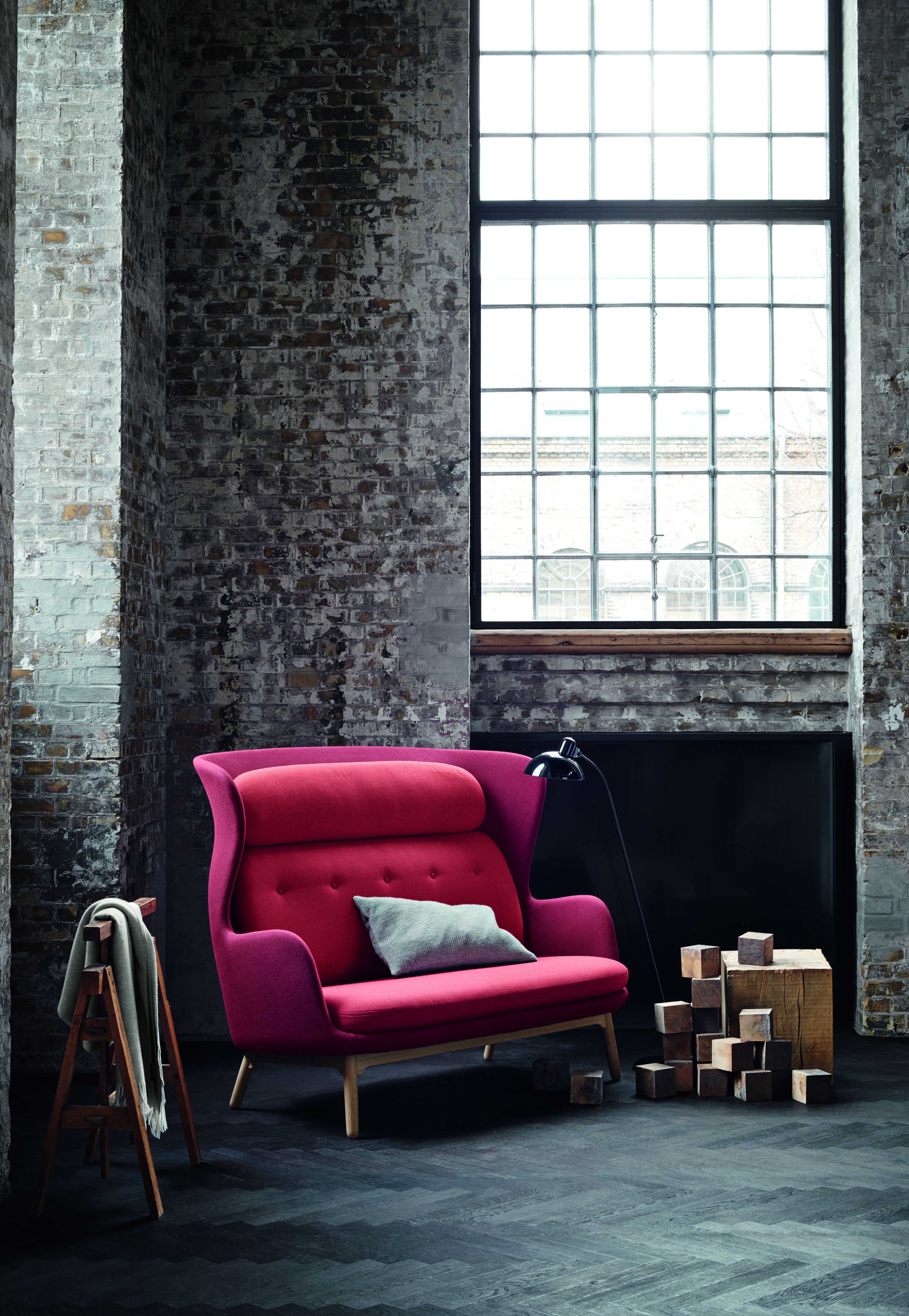 Ro Sessel Holz von Fritz Hansen in Rot vor Backsteinwand und großem Fenster.