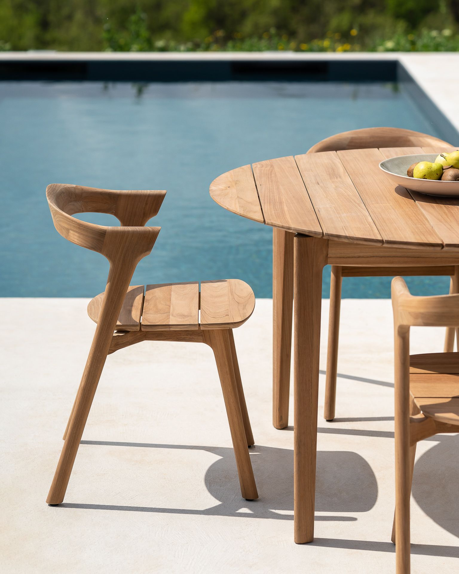 Bok Outdoor Tisch aus Teakholz mit Stühlen neben einem Pool im Freien.
