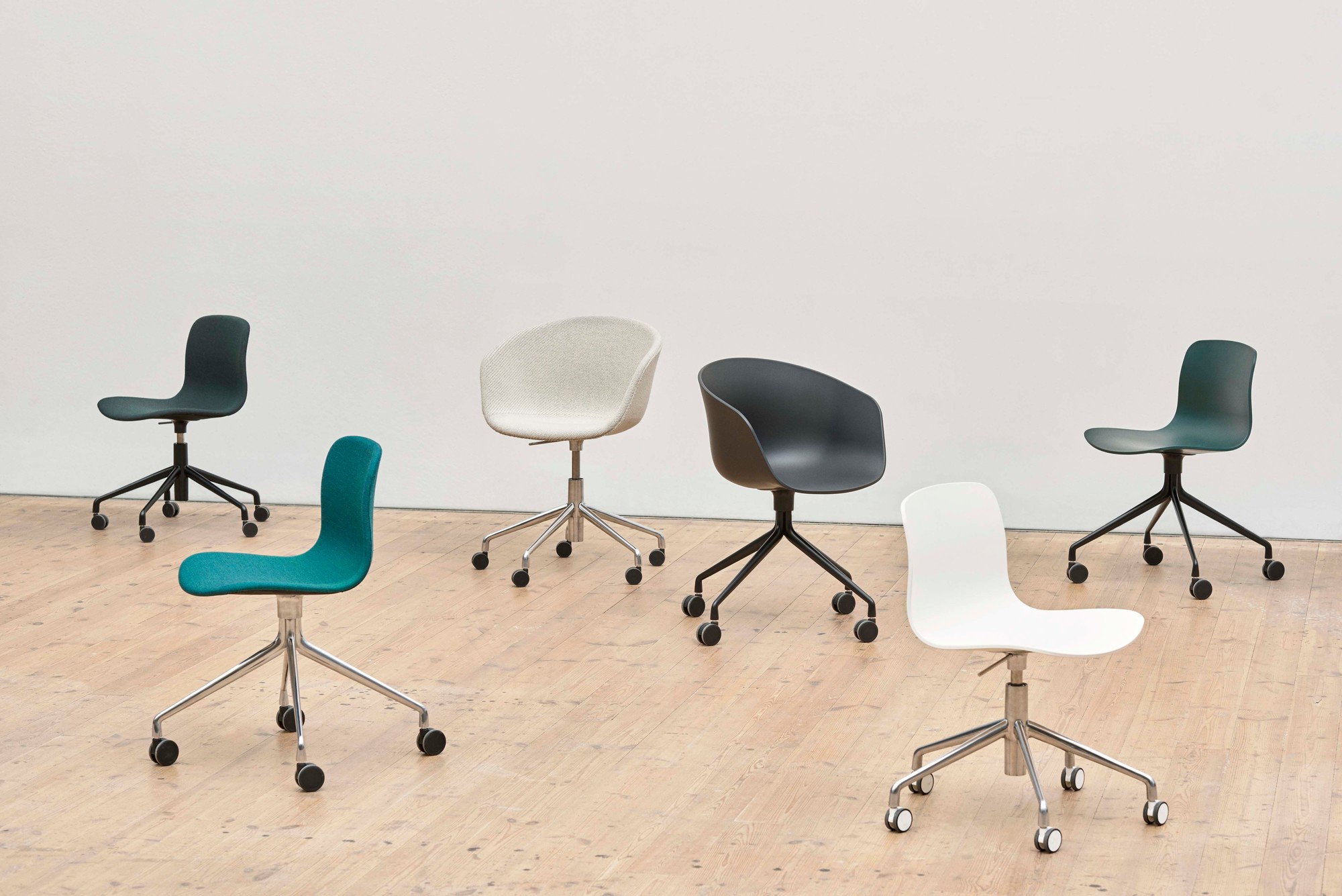 Mehrere Hay About a Chair AAC50 Drehstühle in verschiedenen Farben und Ausführungen auf hellem Holzboden.