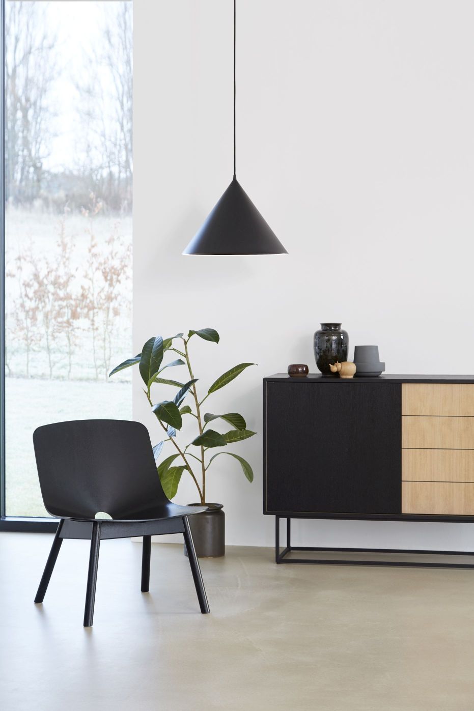 Annular Pendant Pendelleuchte in Schwarz von Woud über einem Sideboard, minimalistisches Wohnzimmerdesign mit Zimmerpflanze und Stuhl.