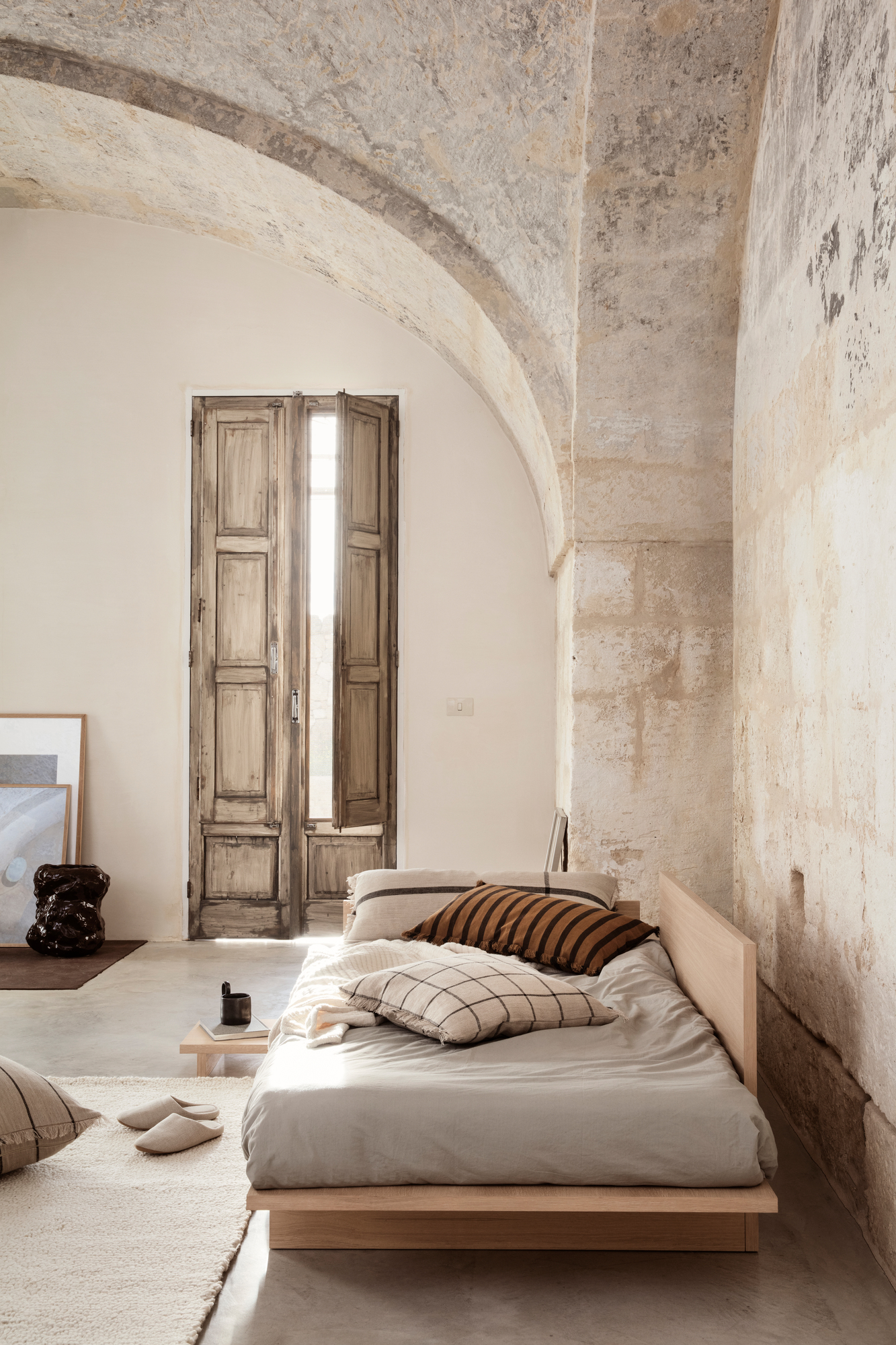Beige Kona Bett von Ferm Living in einem Raum mit Steingewölbe und Holztüren.