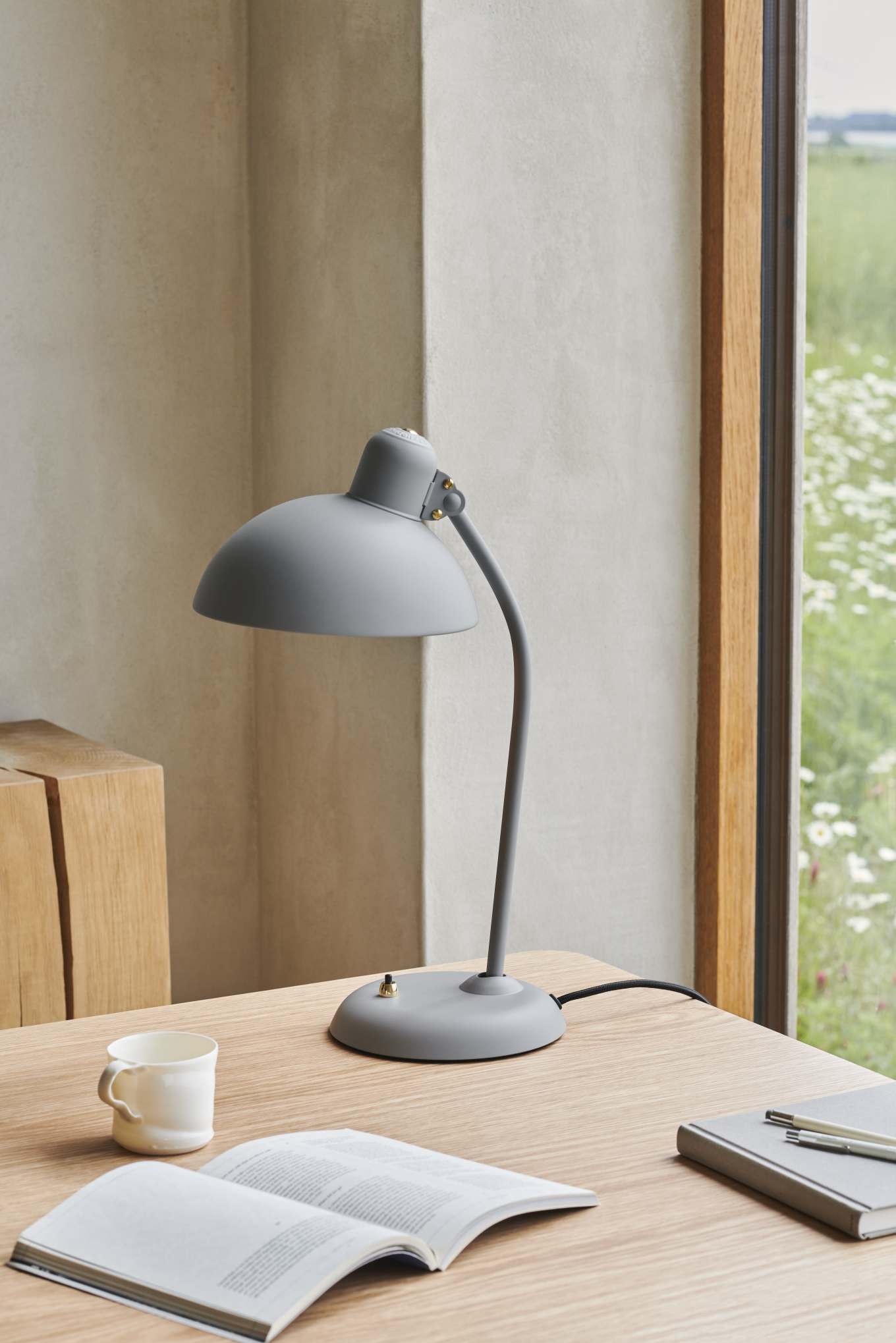 Graue KAISER idell 6556 T Tischleuchte von Fritz Hansen auf einem Schreibtisch mit Buch und Tasse.