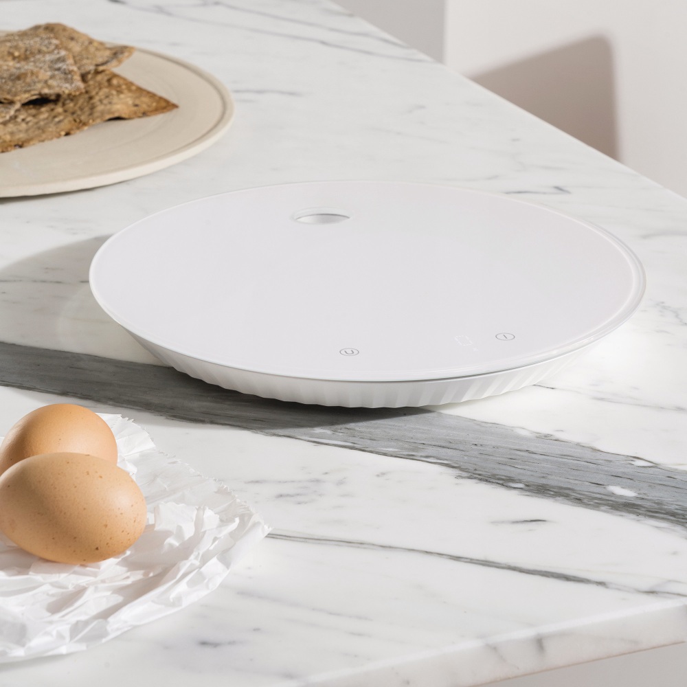 Weiße Alessi Küchenwaage MDL16 Plissé auf Marmor, mit Eiern und Crackern. Digitale Waage.