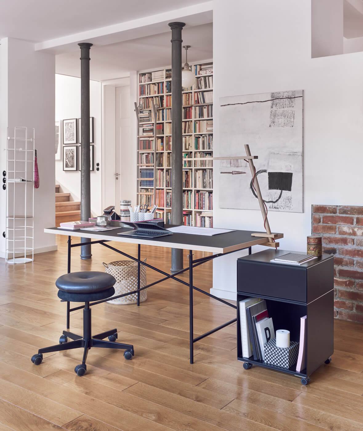 Richard Lampert Eiermann Tischplatte Melamin mit schwarzem Gestell in modernem Wohnraum mit Bücherwand.