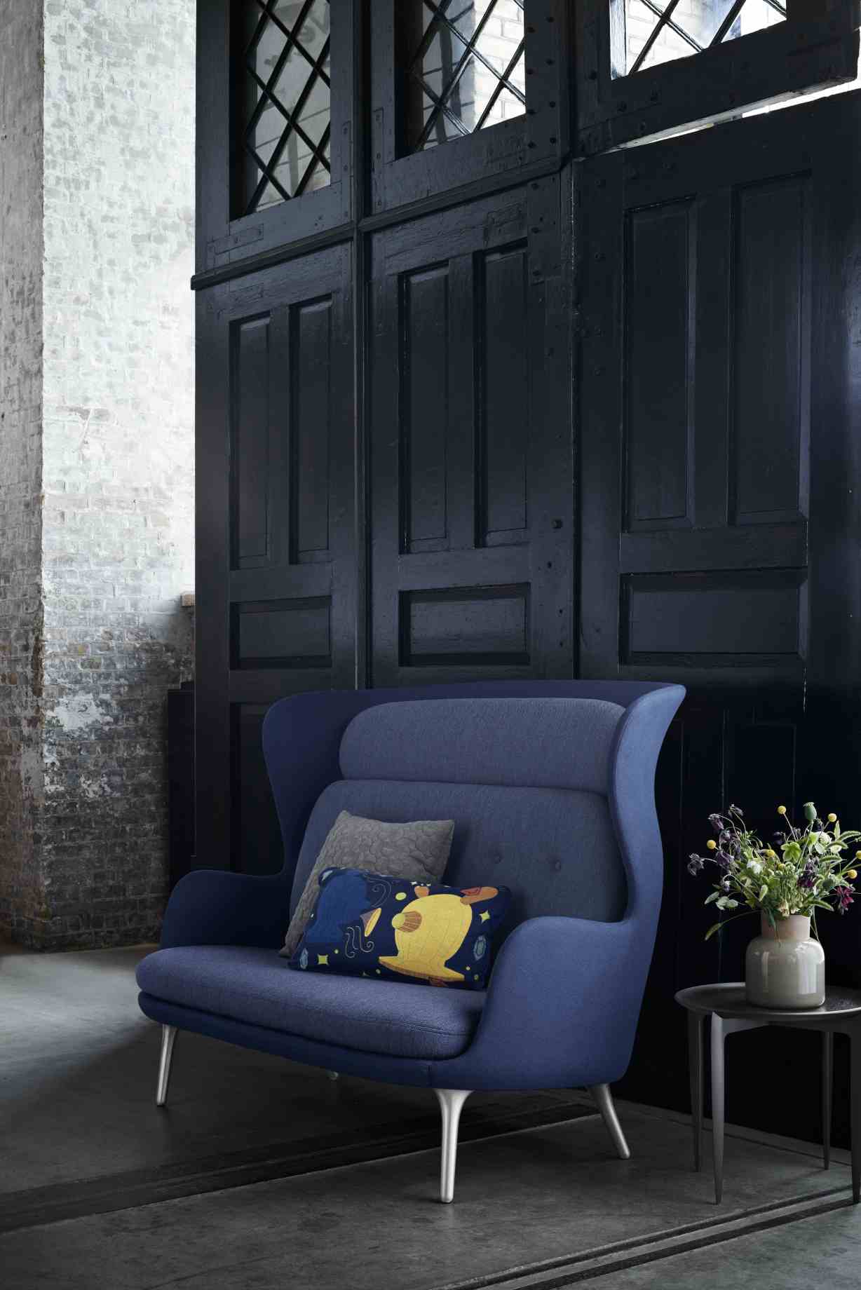 Blaues Ro 2-Sitzer Sofa von Fritz Hansen mit Kissen und Beistelltisch vor dunkler Holzwand.