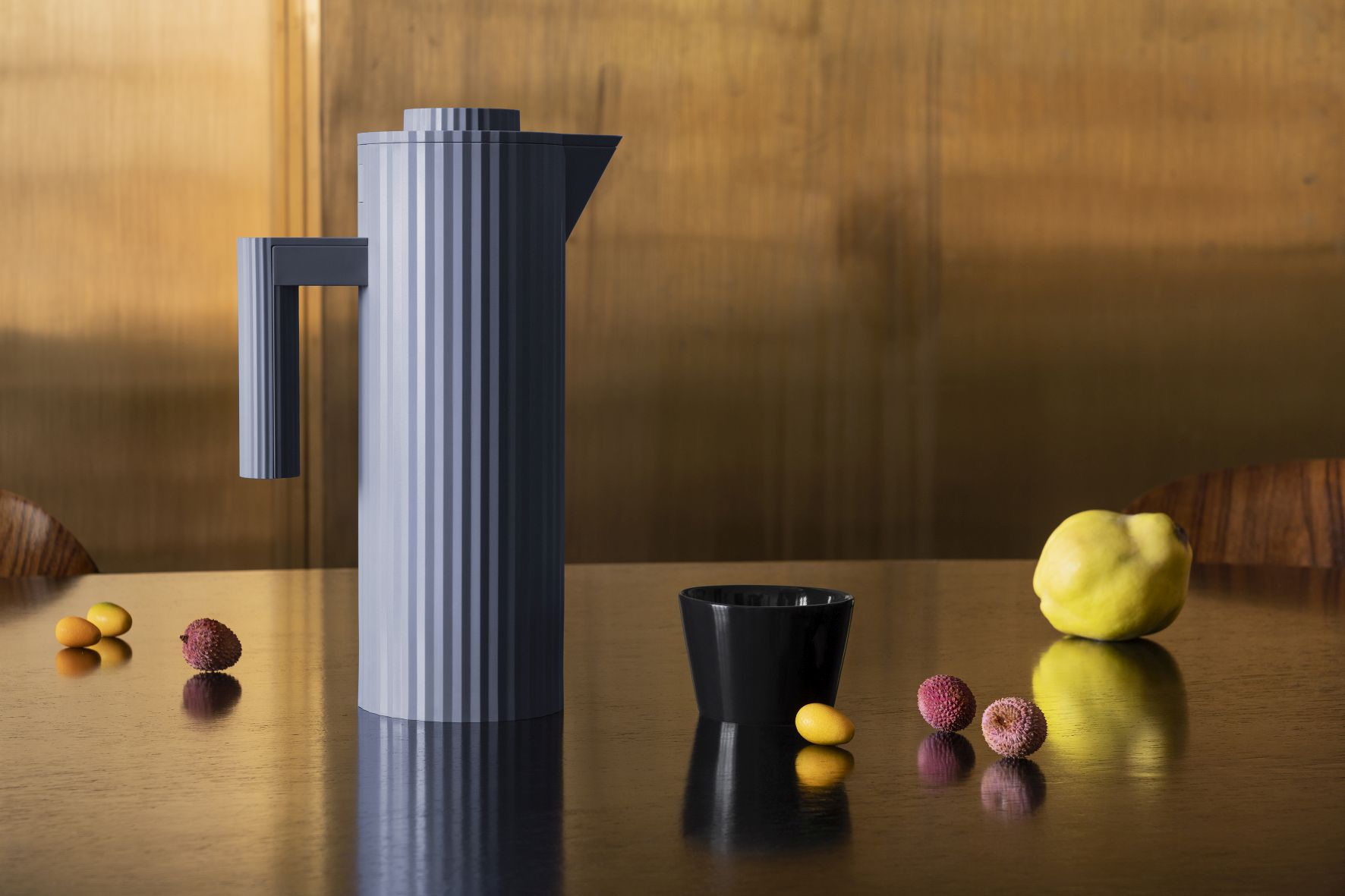 Graue Alessi Plissé Isolierkanne MDL12 auf Tisch mit Tasse und Früchten.