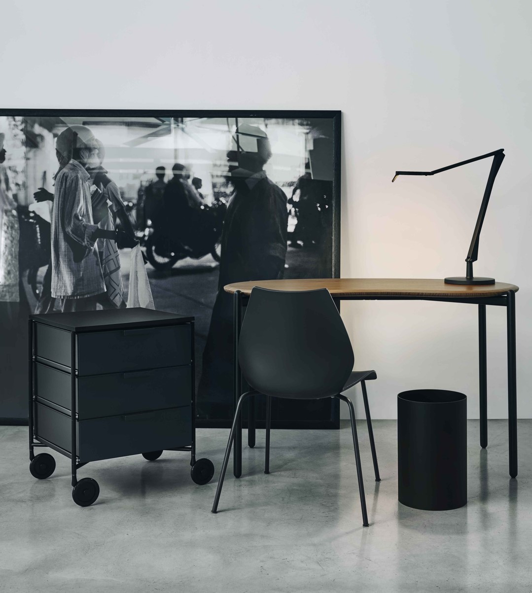 Modernes Büro-Setup mit Holzschreibtisch, schwarzem Rollcontainer, Bürostuhl, Schreibtischlampe und Papierkorb.