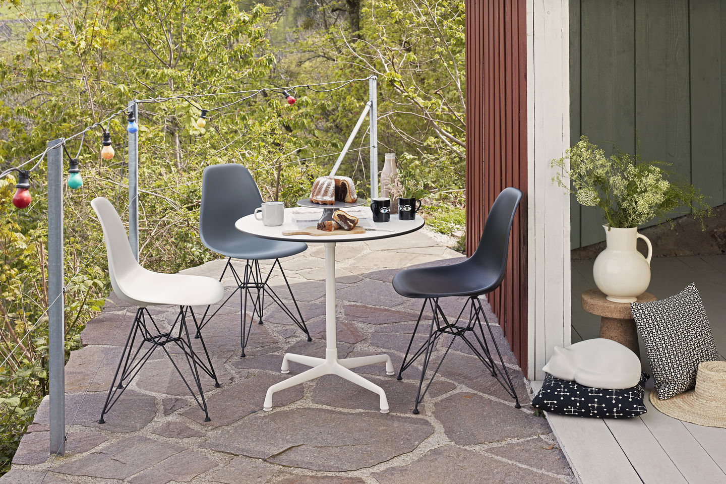 Drei Eames Plastic Side Chairs DSR in Schwarz, Zartrosa und Grau um einen Gartentisch.