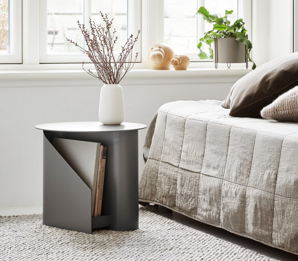 Grauer Beistelltisch mit Magazinhalter, Vase und Dekoration im Wohnzimmer. Moderner Nachttisch für Schlafzimmer.