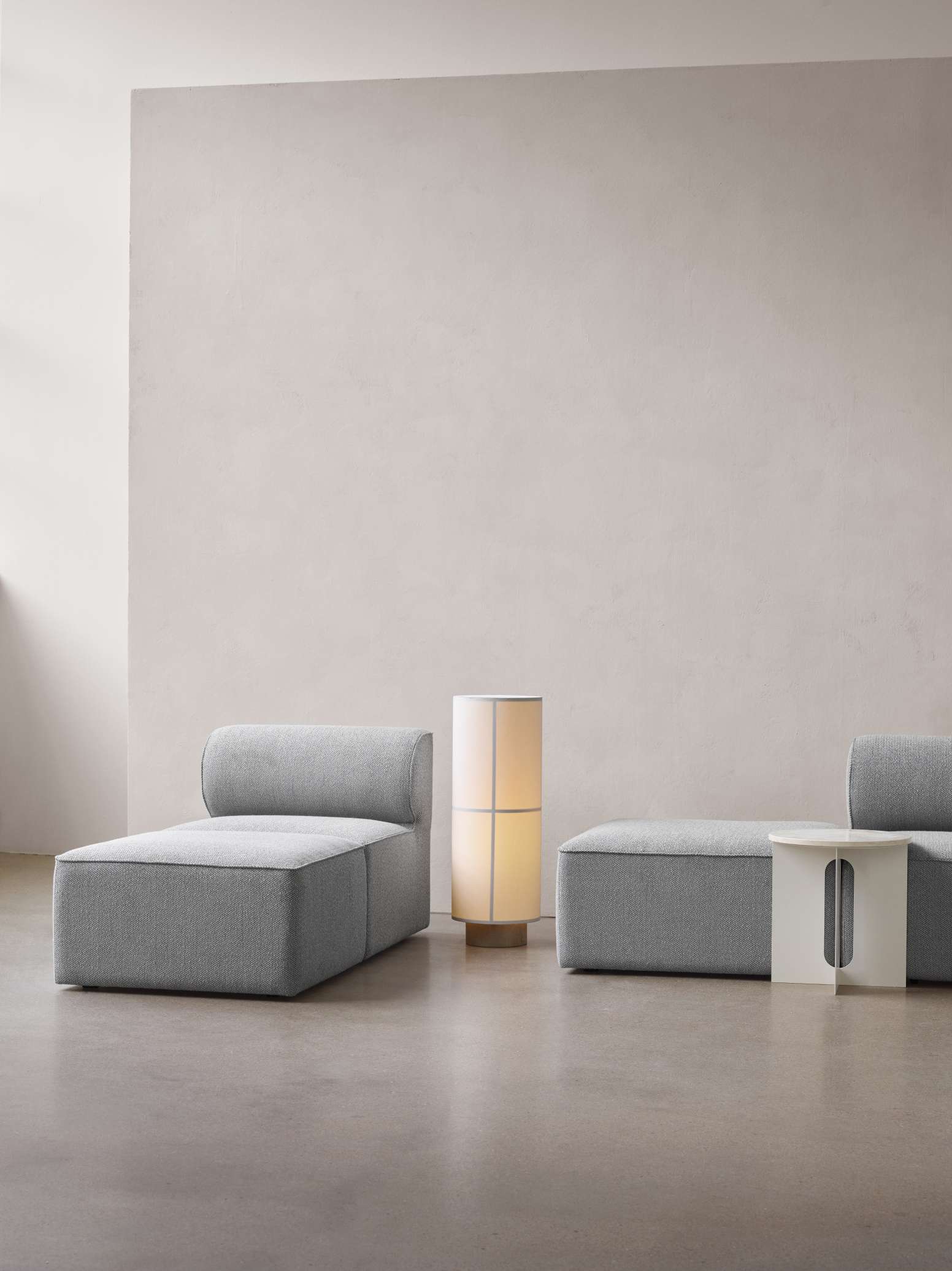Helle Hashira Stehleuchte von Audo neben grauer Couch und Beistelltisch im minimalistischen Wohnzimmer.