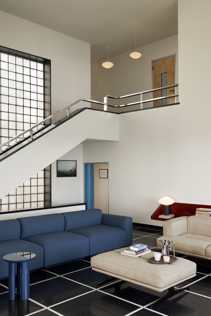 Moderne Wohnraum-Szene mit AndTradition Mist AP15 Pendelleuchten aus Opalglas, die über einer Treppe hängen.