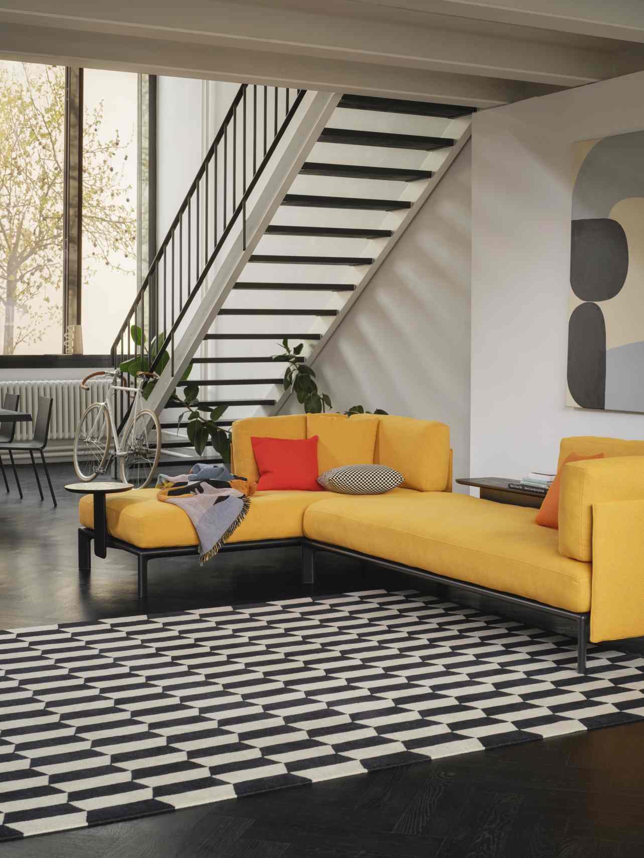 Wohnzimmer mit gelbem Anagram Sofa von Vitra, schwarzem Teppich und Treppe im Hintergrund.