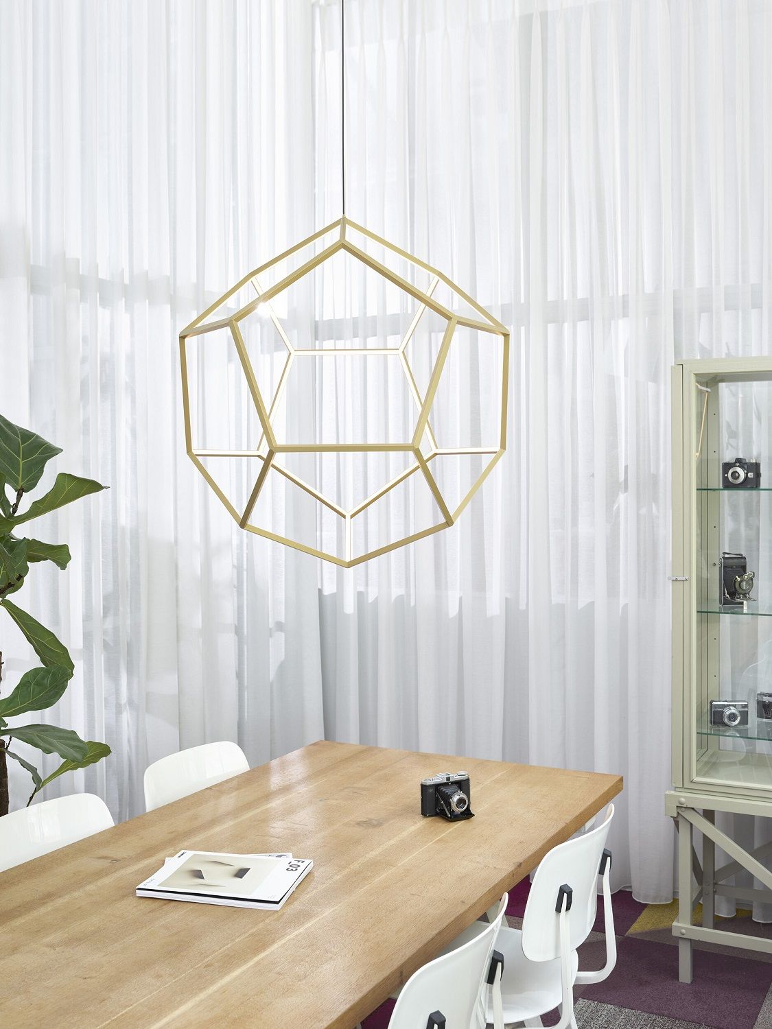 Goldene geometrische Pendelleuchte über Esstisch mit Stühlen und Vintage-Kamera, moderne Innenraumbeleuchtung.