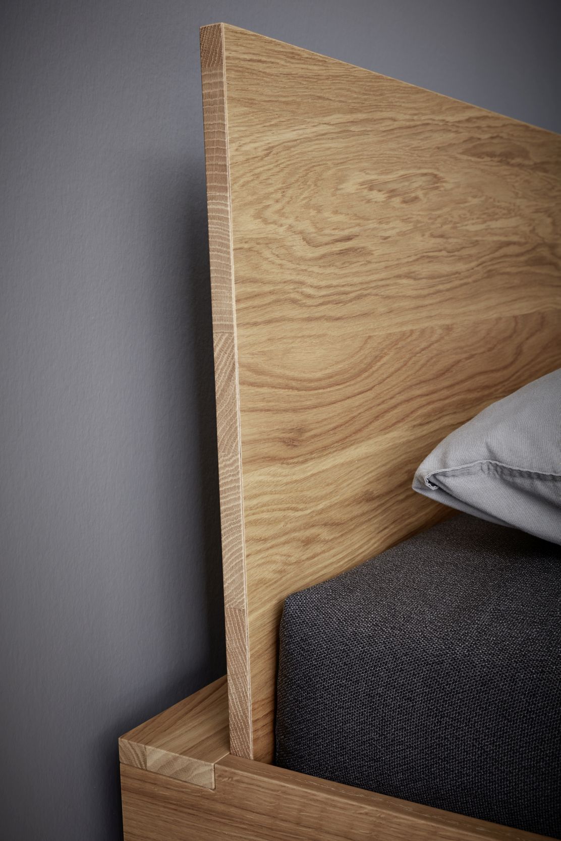 Detailaufnahme vom Müller Möbelwerkstätten Flai Bett Kopfteil aus Eiche mit grauem Kissen.
