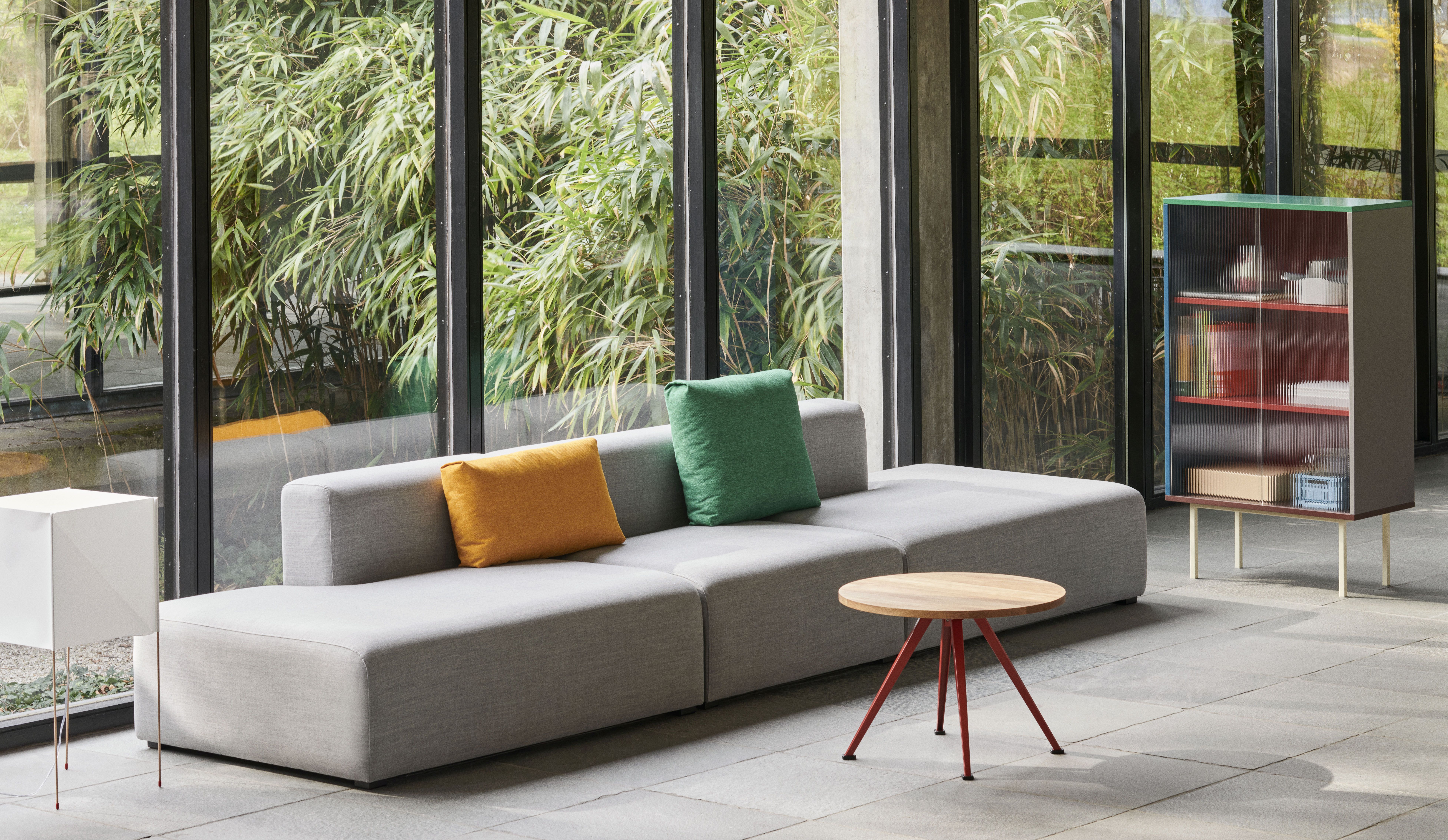 Graues Mags Sofa mit Kissen, Beistelltisch und Schrank vor Fenster mit Bambus.