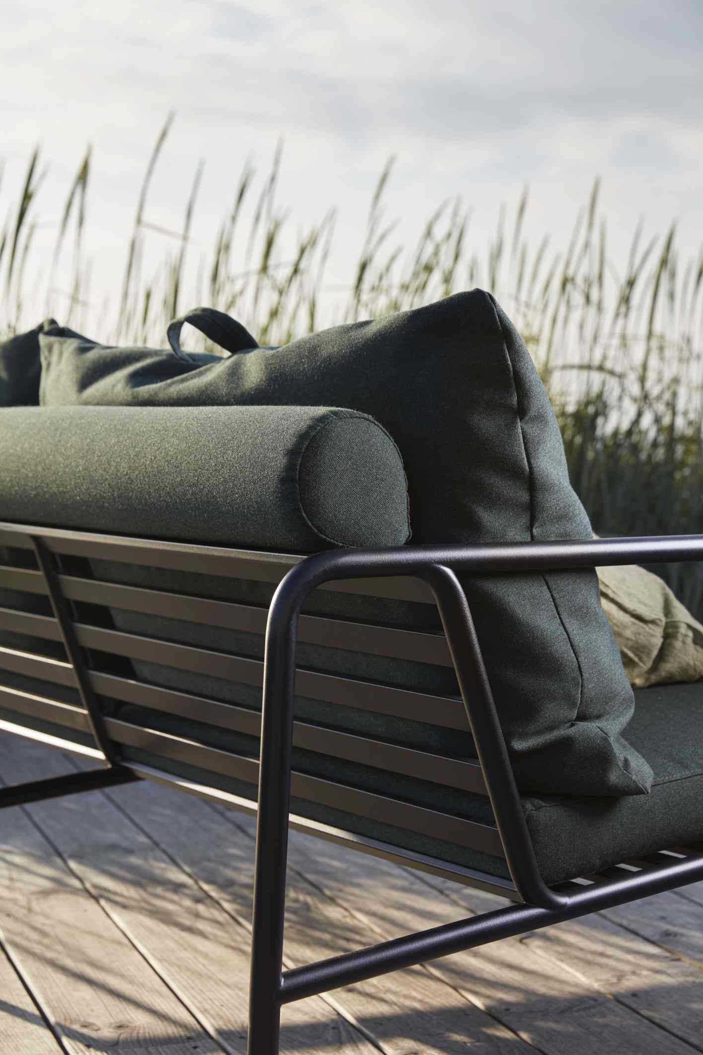 Detailaufnahme des Avon Outdoor Sofas von Houe mit dunkelgrünen Kissen und schwarzem Metallrahmen.