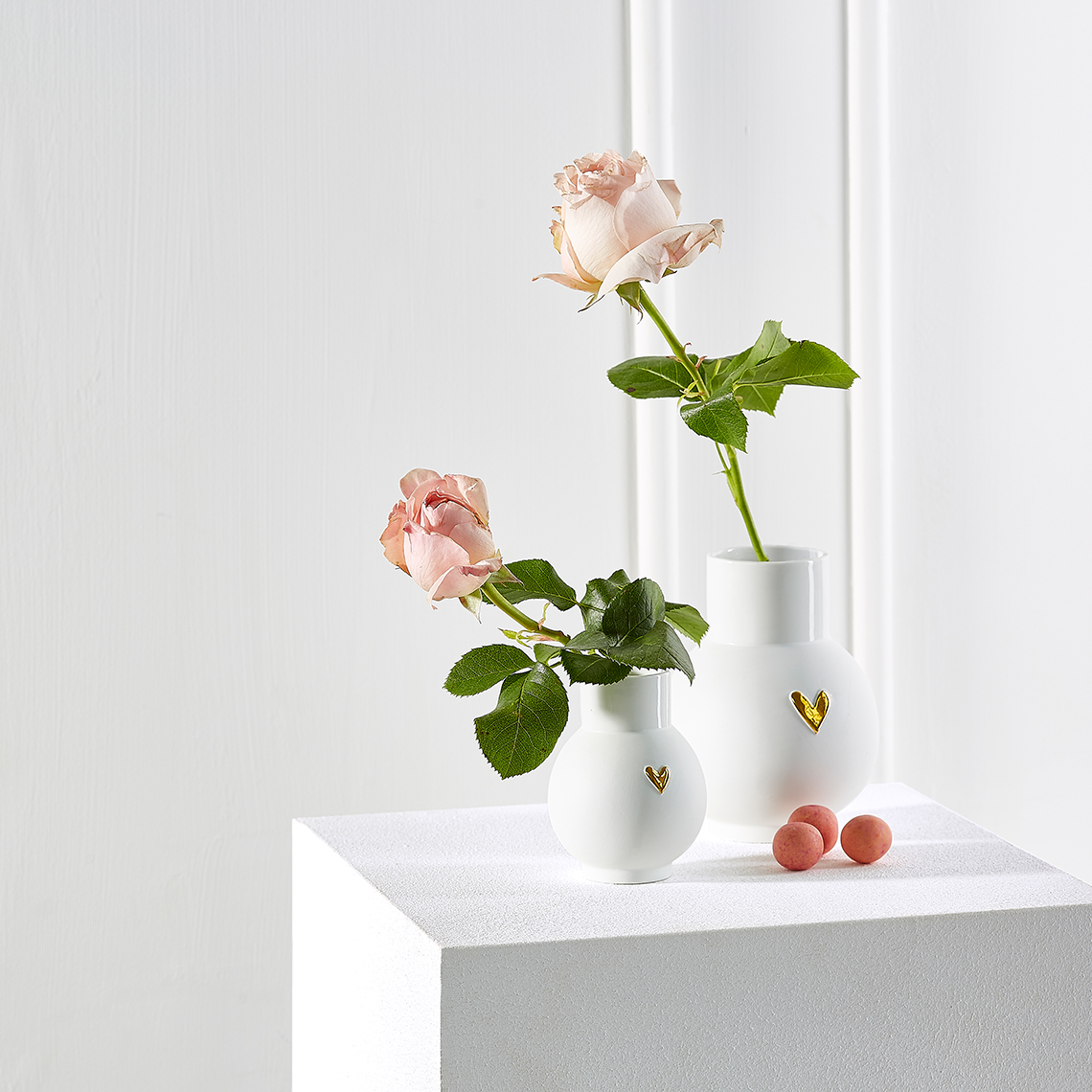 Zwei weiße Kugelvasen mit goldenen Herzen und Rosen, Dekoration für Zuhause.