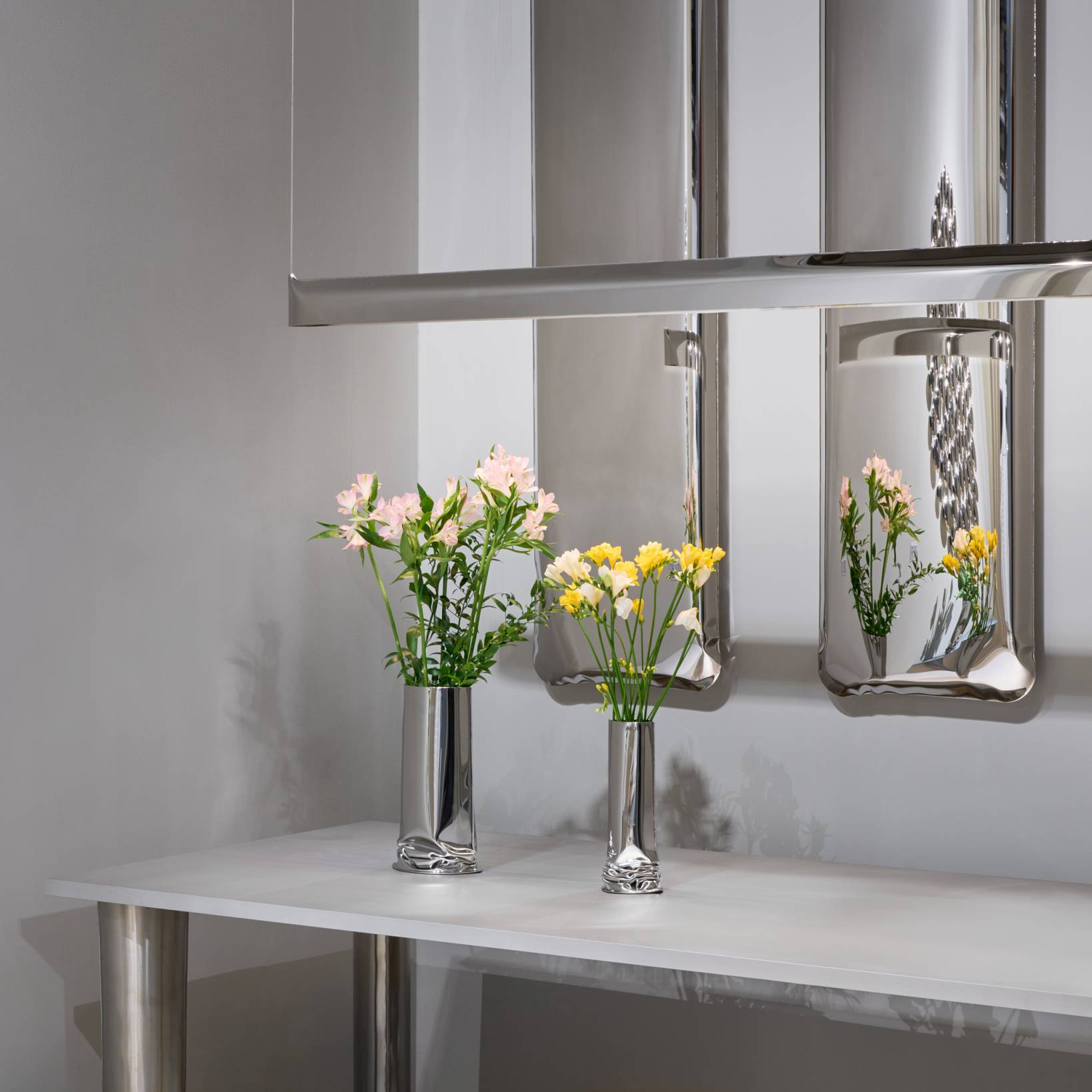 Crash Table Esstisch Zieta: Detailansicht des modernen Designtisches mit Blumenvasen und reflektierenden Wandelementen in Silber.