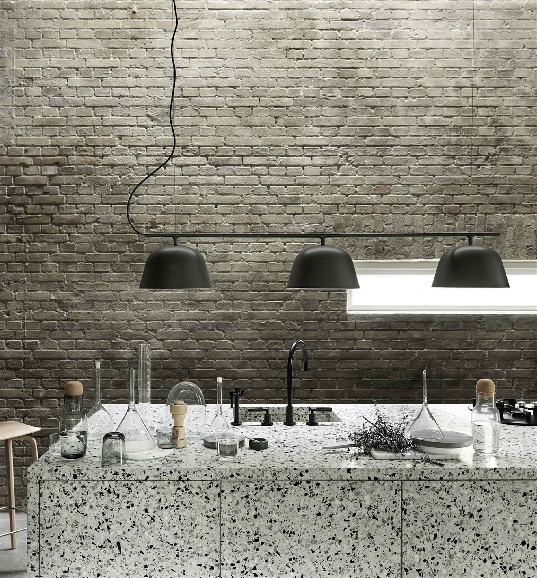 Schwarze Ambit Rail Lamp Pendelleuchte von Muuto über einer Kücheninsel mit Terrazzo-Arbeitsplatte vor einer Backsteinwand.