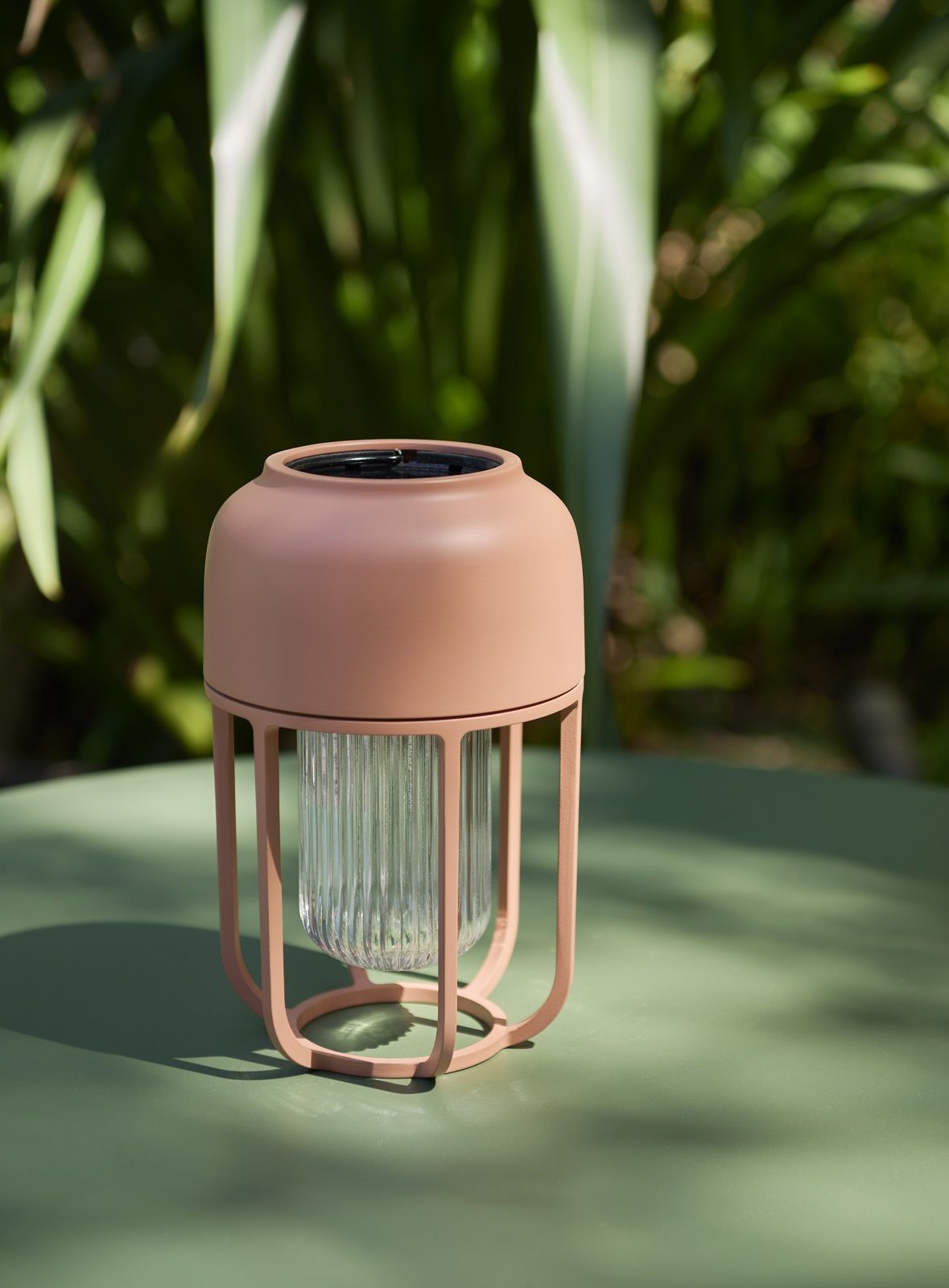 Nahaufnahme der Houe LIGHT No.1 Solarleuchte in Rosa auf einem grünen Tisch im Freien.