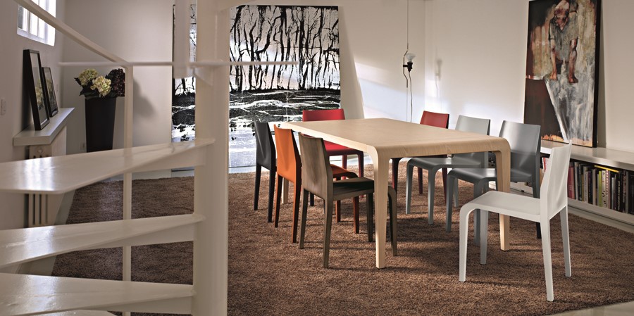 Esszimmer mit Holztisch und Laleggera Stühlen von Alias in verschiedenen Farben auf braunem Teppich.