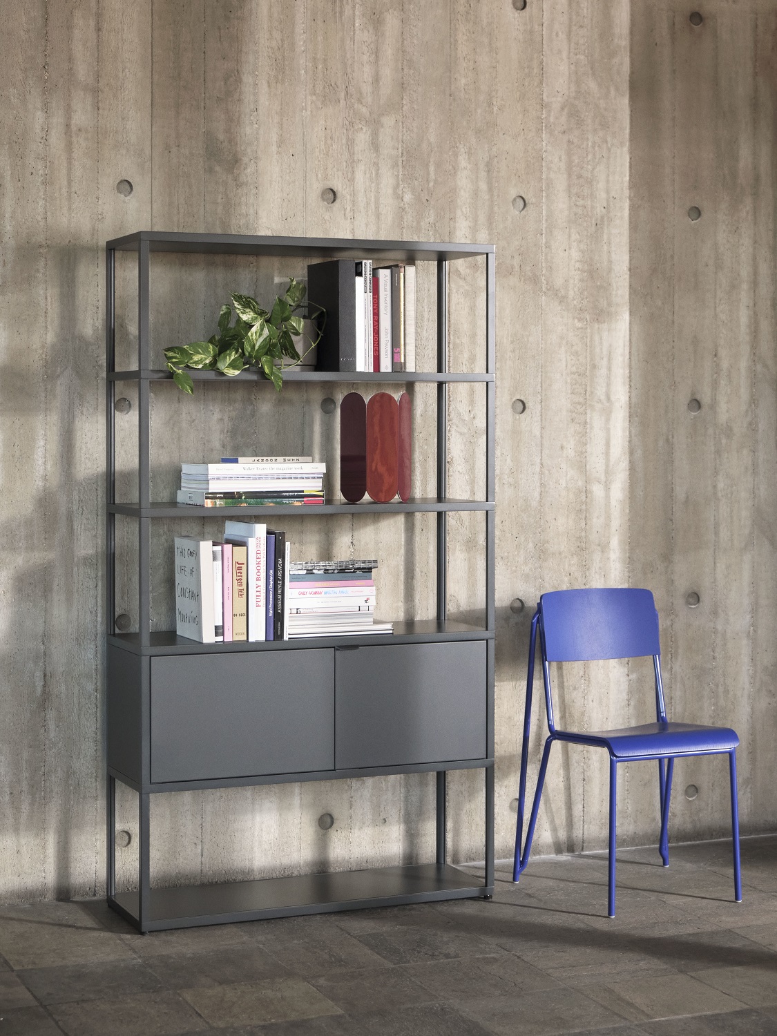 Graues New Order Sideboard von Hay mit Regalen, Schrankfächern und blauer Stuhl vor Betonwand.