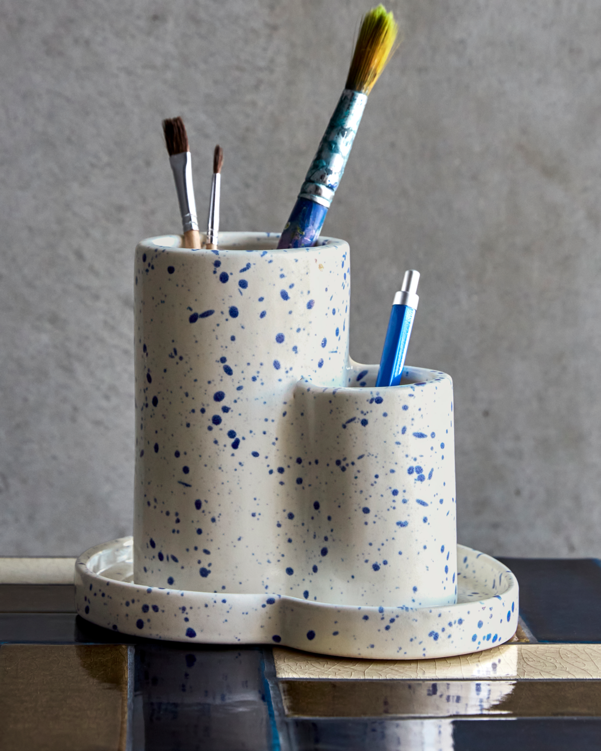 House Doctor Organizer Sand, Keramik Stiftehalter mit blauen Sprenkeln, gefüllt mit Pinseln und Stift.