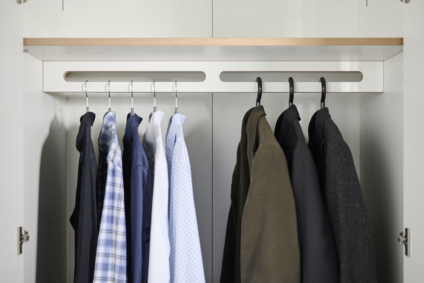 Innenansicht Tojo-Schrank Grundmodul mit Kleiderstange und hängenden Hemden und Jacken in verschiedenen Farben.