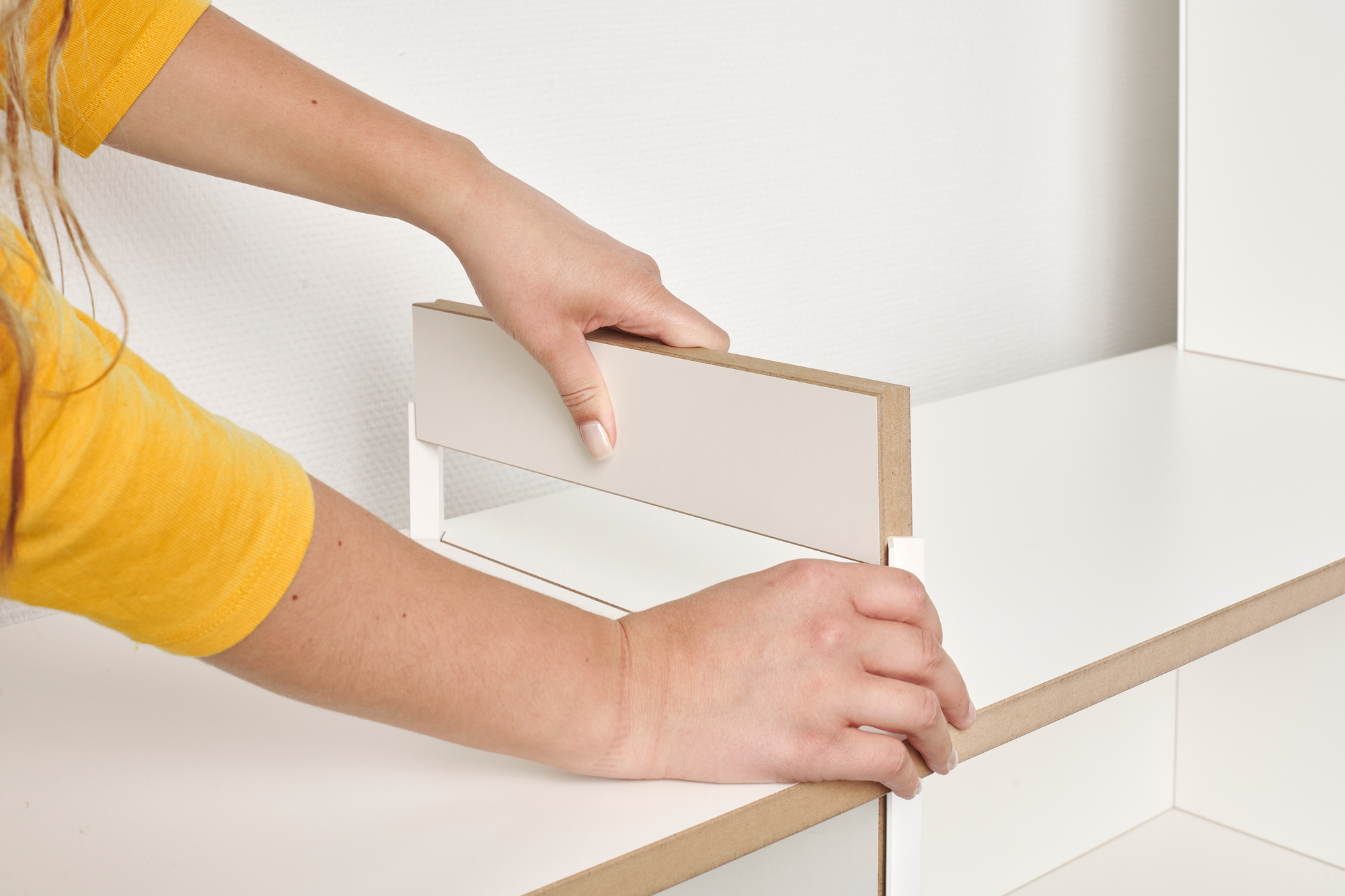 Hände montieren ein weißes Tojo Mehrfach Regal Anbaumodul, flexibles Regalsystem für Wohnzimmer und Büro.