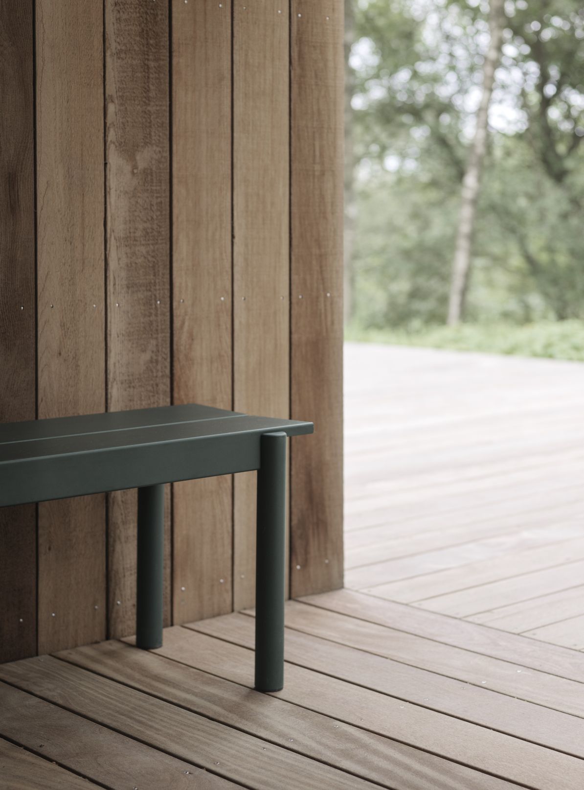 Grüne Muuto Linear Steel Bank für den Außenbereich, 110 cm breit, vor Holzwand und Holzboden.