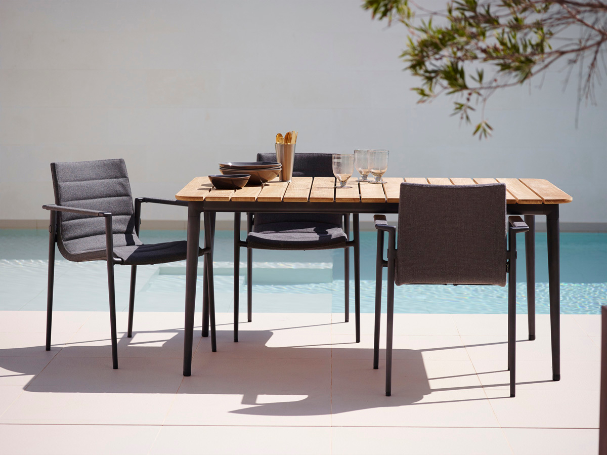 Cane-Line Core Outdoor Esstisch aus Teakholz mit grauen Stühlen am Pool, gedeckt mit Geschirr.