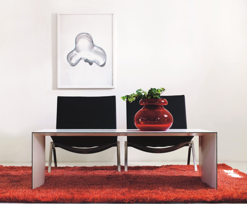 Moderner Thinner Tisch von Karl Andersson & Soener mit roter Vase und Stühlen auf rotem Teppich.