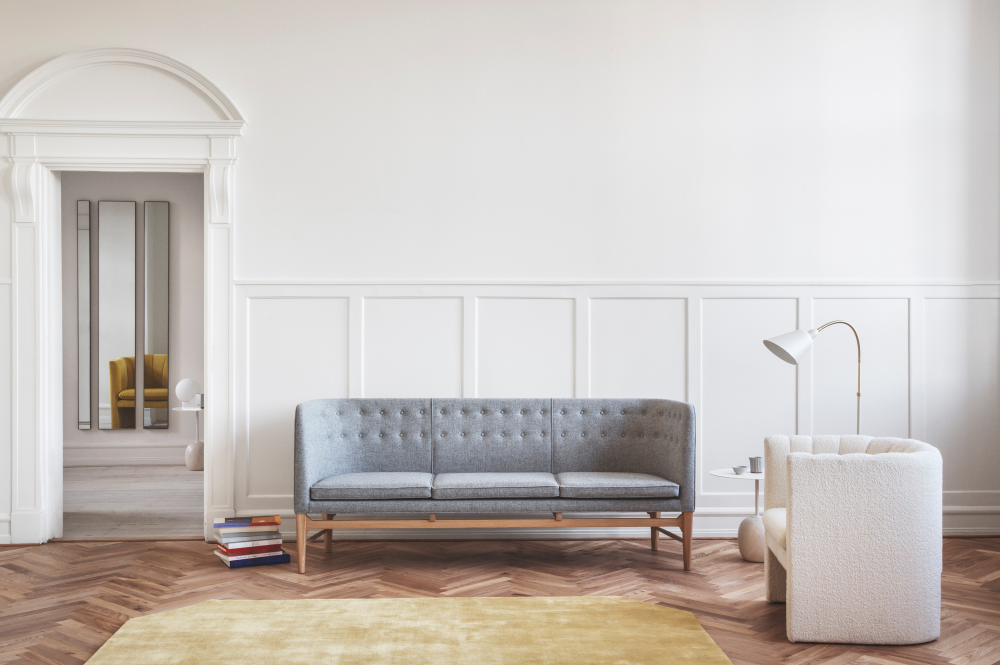 Graues Mayor Sofa von AndTradition im skandinavischen Wohnzimmer mit Sessel, Lampe und Bücherstapel.