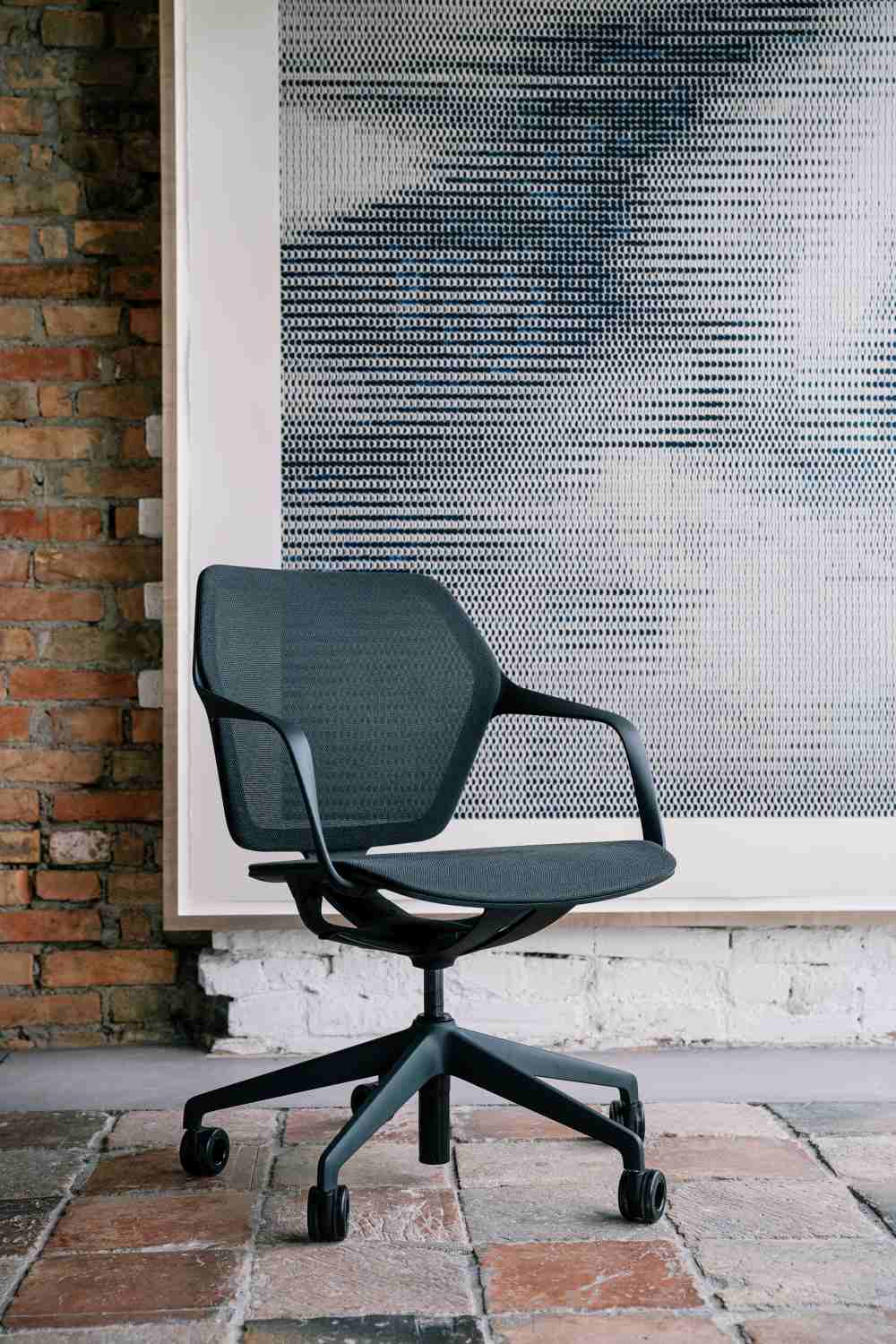 Ray Work 9220 Bürodrehstuhl von Brunner, ergonomischer Schreibtischstuhl mit Armlehnen und schwarzem Netzrücken vor Backsteinwand.